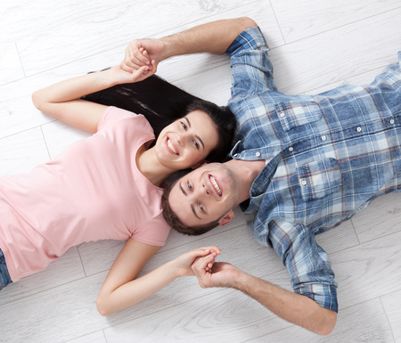 Happy young couple, lying on the floor, look at each other and dream of furniture for a new apartment. Mock upの写真素材