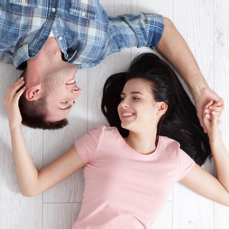 Happy young couple, lying on the floor, look at each other and dream of furniture for a new apartment. Mock upの写真素材