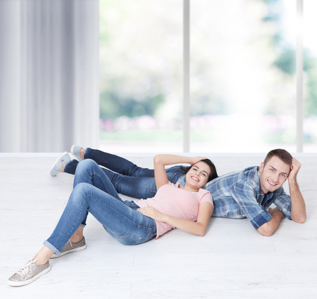 Happy young couple, lying on the floor, look at each other and dream of furniture for a new apartment. Mock upの写真素材