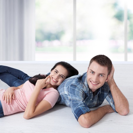 Happy young couple, lying on the floor, look at each other and dream of furniture for a new apartment. Mock upの写真素材