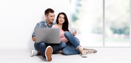 Happy young couple sitting on the floor with a laptop looking for their new home and furniture. Mock upの写真素材