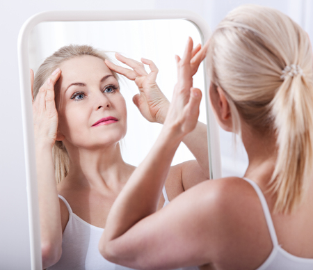 Middle aged woman looking at wrinkles in mirror. Plastic surgery and collagen injections. Makeup. Macro face. Selective focusの写真素材
