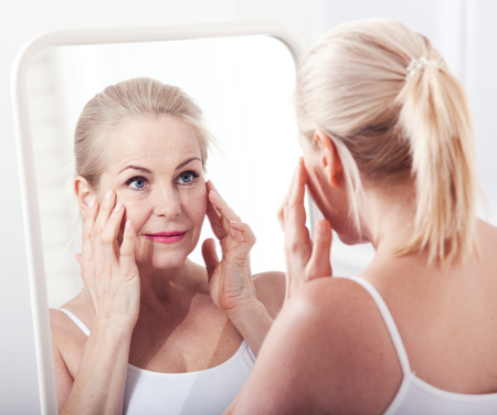 Middle aged woman looking at wrinkles in mirror. Plastic surgery and collagen injections. Makeup. Macro face. Selective focusの写真素材