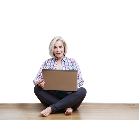 Smiling beautiful middle-aged woman sitting on the floor with laの写真素材