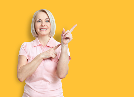 Friendly smiling middle aged woman pointing at copyspace isolateの写真素材