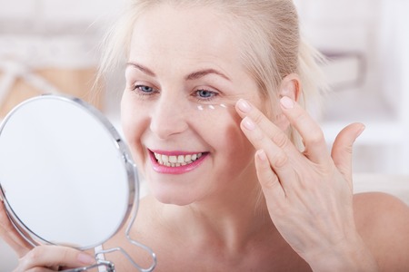 Middle aged woman looking at wrinkles in mirror. Plastic surgery and collagen injections. Makeup. Macro face. Selective focusの写真素材