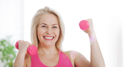 Happy middle aged woman lifting dumbbells at home in the living roomの写真素材