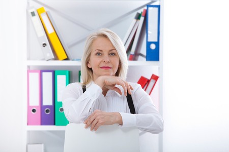 Lovely middle-aged blond woman with a beaming smile sitting at office looking at the cameraの写真素材