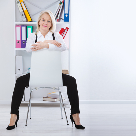 Lovely middle-aged blond woman with a beaming smile sitting at office looking at the cameraの写真素材