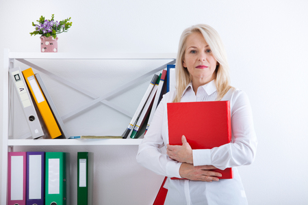 Successful business woman looking confident and smiling. business woman in blue shirt looking friendly into camera standing near window in officeの写真素材
