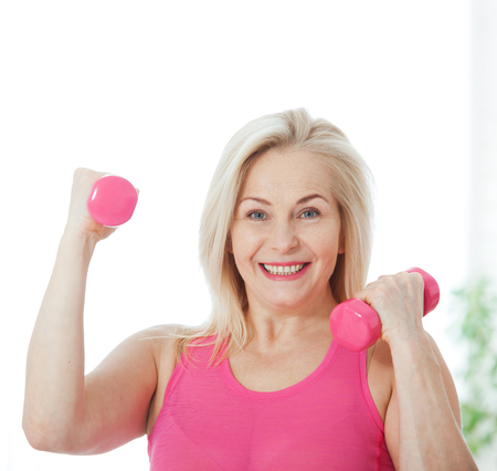 Happy middle aged woman lifting dumbbells at home in the living roomの写真素材