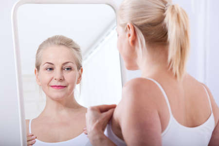 Forty years old woman looking at wrinkles in mirror. Plastic surgery and collagen injections. Makeup. Macro face. Selective focusの写真素材