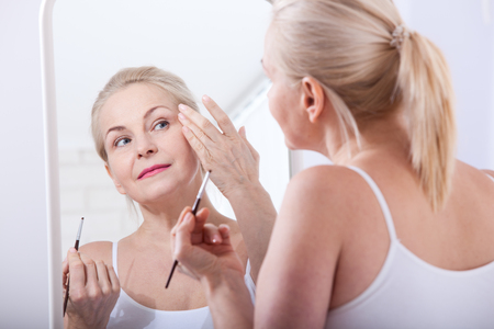 Forty years old woman looking at wrinkles in mirror. Plastic surgery and collagen injections. Makeup. Macro face. Selective focusの写真素材