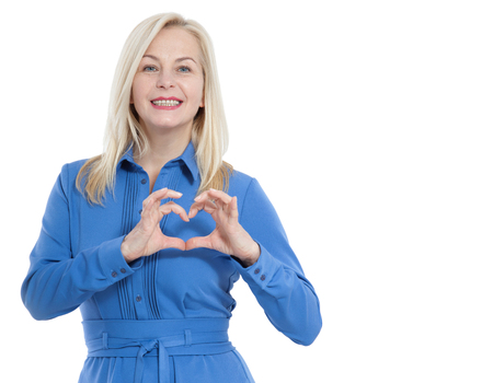 Friendly smiling middle aged woman in blue dress looks at the camera and shows a gesture I love you isolated on white.の写真素材