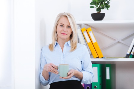 Smiling middle aged businessman with a cup of coffee in the office. Coffee break.の写真素材