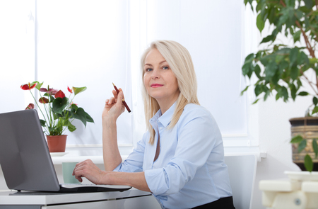 Pretty middle aged business woman working on computer in her officeの写真素材