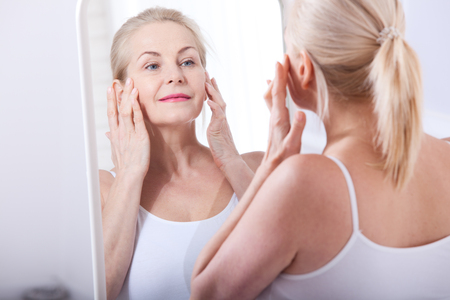 Forty years old woman looking at wrinkles in mirror. Plastic surgery and collagen injections. Makeup. Macro face. Selective focusの写真素材