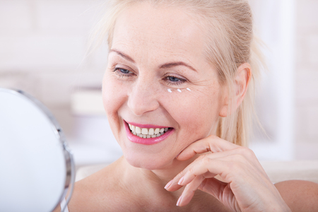 Forty years old woman looking at wrinkles in mirror. Plastic surgery and collagen injections. Makeup. Macro face. Selective focusの写真素材