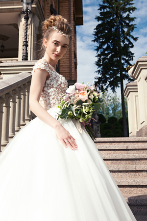 Young bride in a white dress with a beautiful wedding bouquet on a marble staircase in an old castle. Bride holds a wedding bouquet, wedding beautiful dress, wedding details. Wedding ceremony concept.の写真素材