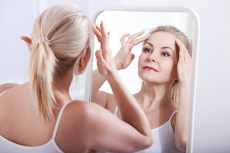 Middle aged woman looking at wrinkles in mirror. Plastic surgery and collagen injections. Makeup. Macro face. Selective focusの写真素材