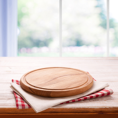 Empty pizza board with tablecloth on the table and kitchen window blurredの写真素材