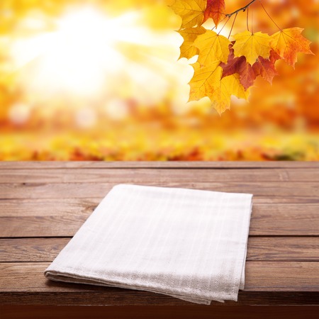 Empty wooden deck table with tablecloth over bokeh autumn leavesの写真素材