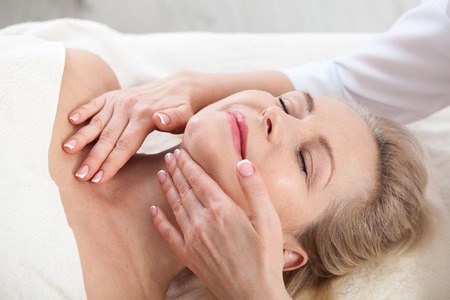 Face massage in spa macro. Attractive woman with close eyes taking skin care.の写真素材