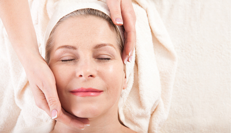 Face massage in spa macro. Attractive woman with close eyes taking skin care.の写真素材