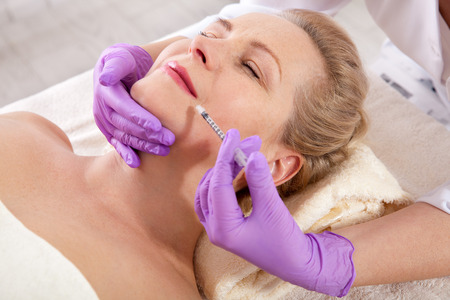 Middle aged woman gets cosmetic injection in her lips.の写真素材
