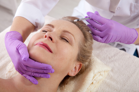 Middle aged woman gets cosmetic injection in her forehead.の写真素材