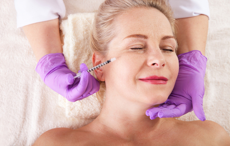 Middle aged woman gets cosmetic injection in the face.の写真素材