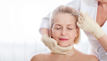 Middle aged woman gets cosmetic injection in her forehead.の写真素材