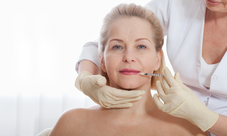 Middle aged woman gets cosmetic injection in the face.の写真素材