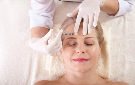 Middle aged woman gets cosmetic injection in her forehead.の写真素材