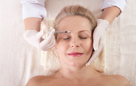 Middle aged woman gets cosmetic injection in her forehead.の写真素材