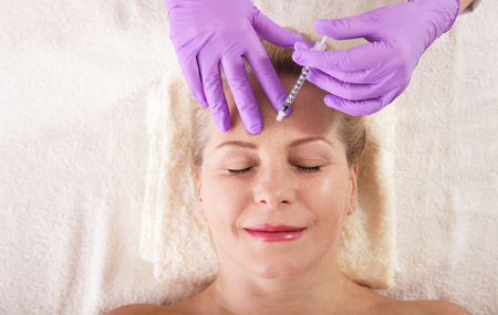 Middle aged woman gets cosmetic injection in her forehead.の写真素材