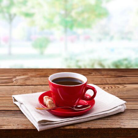 Red cup of tasty coffee on napkin, on wooden table.の写真素材
