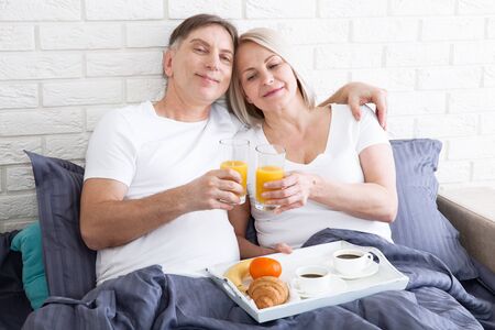 Happy middle aged couple having breakfast in the bed at hotelの写真素材