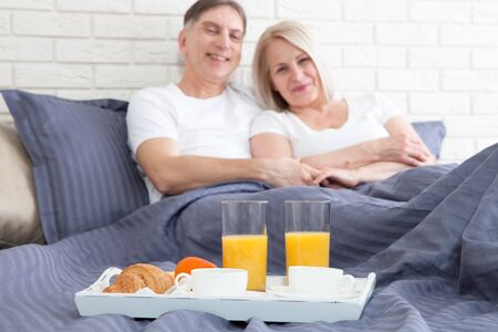 Happy middle aged couple having breakfast in the bed at hotelの写真素材