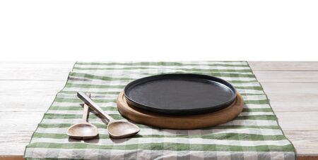 Black plate or tray, or pizza board, with tablecloth on wooden table. Top view mockupの写真素材