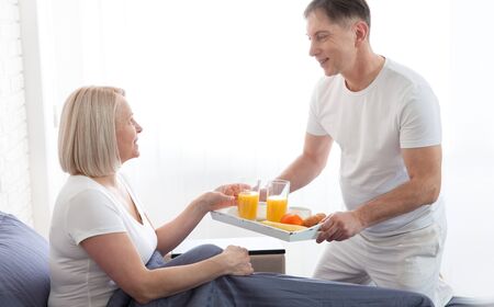 Attractive man holding breakfast tray to happy relaxed woman in bedの写真素材