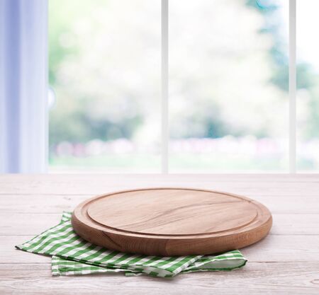 Empty pizza board with tablecloth on the table and kitchen window blurred backgroundの写真素材