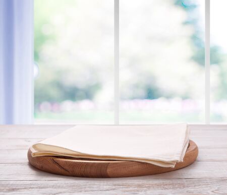Empty pizza board with tablecloth on the table and kitchen window blurred backgroundの写真素材
