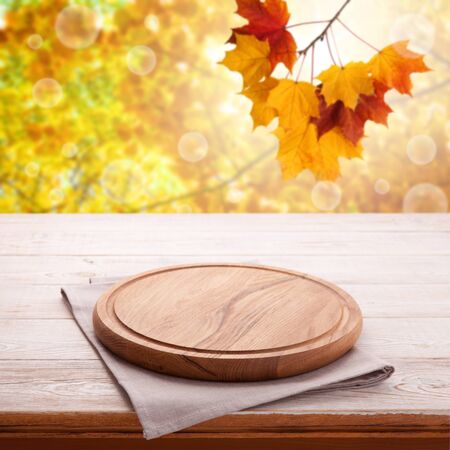 Wooden table with empty board for pizza and tablecloth. Autumn background top view mock up. Selective focus.の写真素材