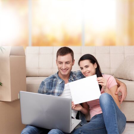 Beautiful young couple using laptop communicates in video chat. A woman is smiling and showing blank piece of paper.の写真素材
