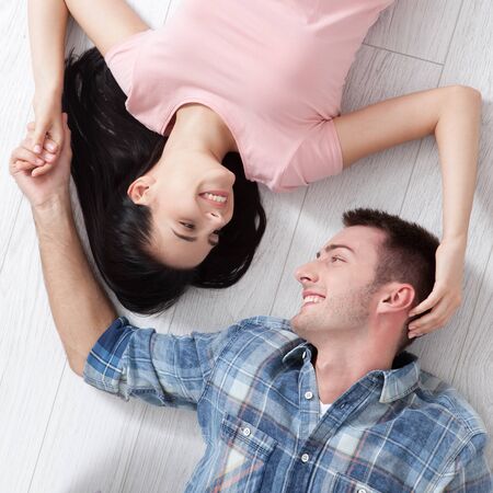 Happy young couple, lying on the floor, look at each other and dream of furniture for a new apartment. Mock upの写真素材