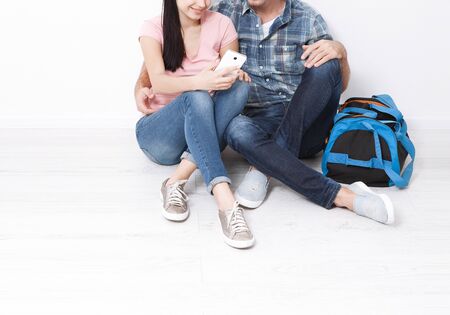 A woman and a man are sitting in a new apartment using a smartphone. A young couple chooses a wedding trip.の写真素材