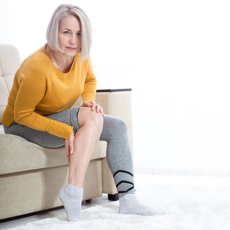Middle-aged woman suffering from pain in leg at home, closeup. Physical injury concept.の写真素材