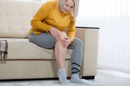 Middle-aged woman suffering from pain in leg at home, closeup. Physical injury concept.の写真素材