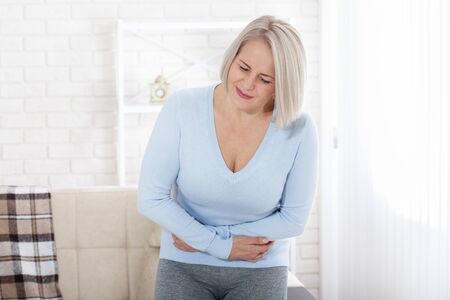 Middle aged woman suffering from abdominal pain while at homeの写真素材